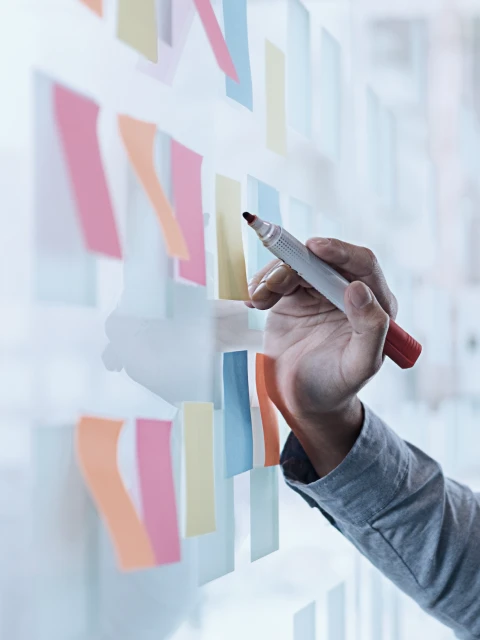 ホワイトボードに貼られた付箋にペンで書き込む手